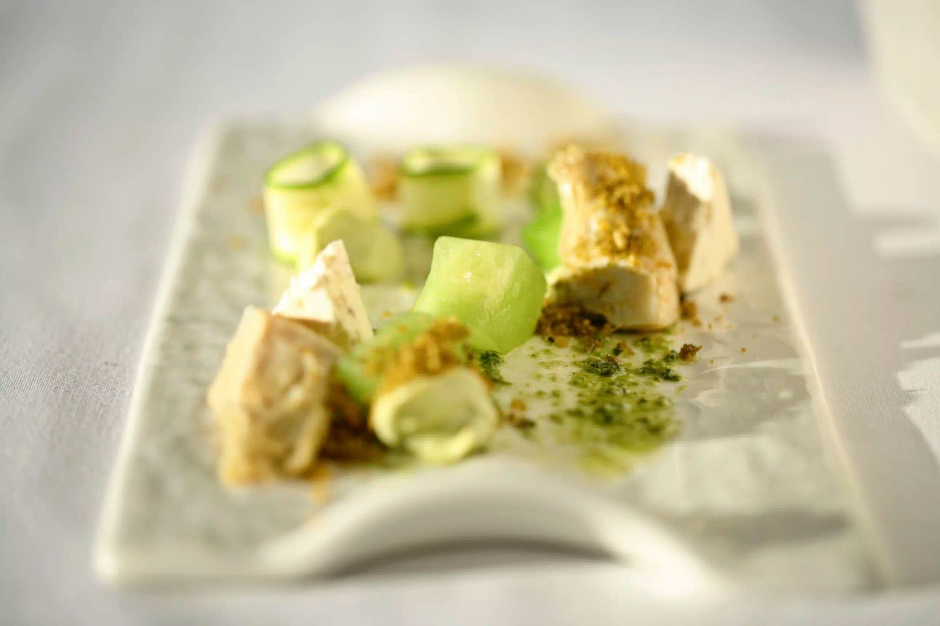 Plated gourmet appetizer with cucumber rolls, herbs, and creamy sauce on a white dish