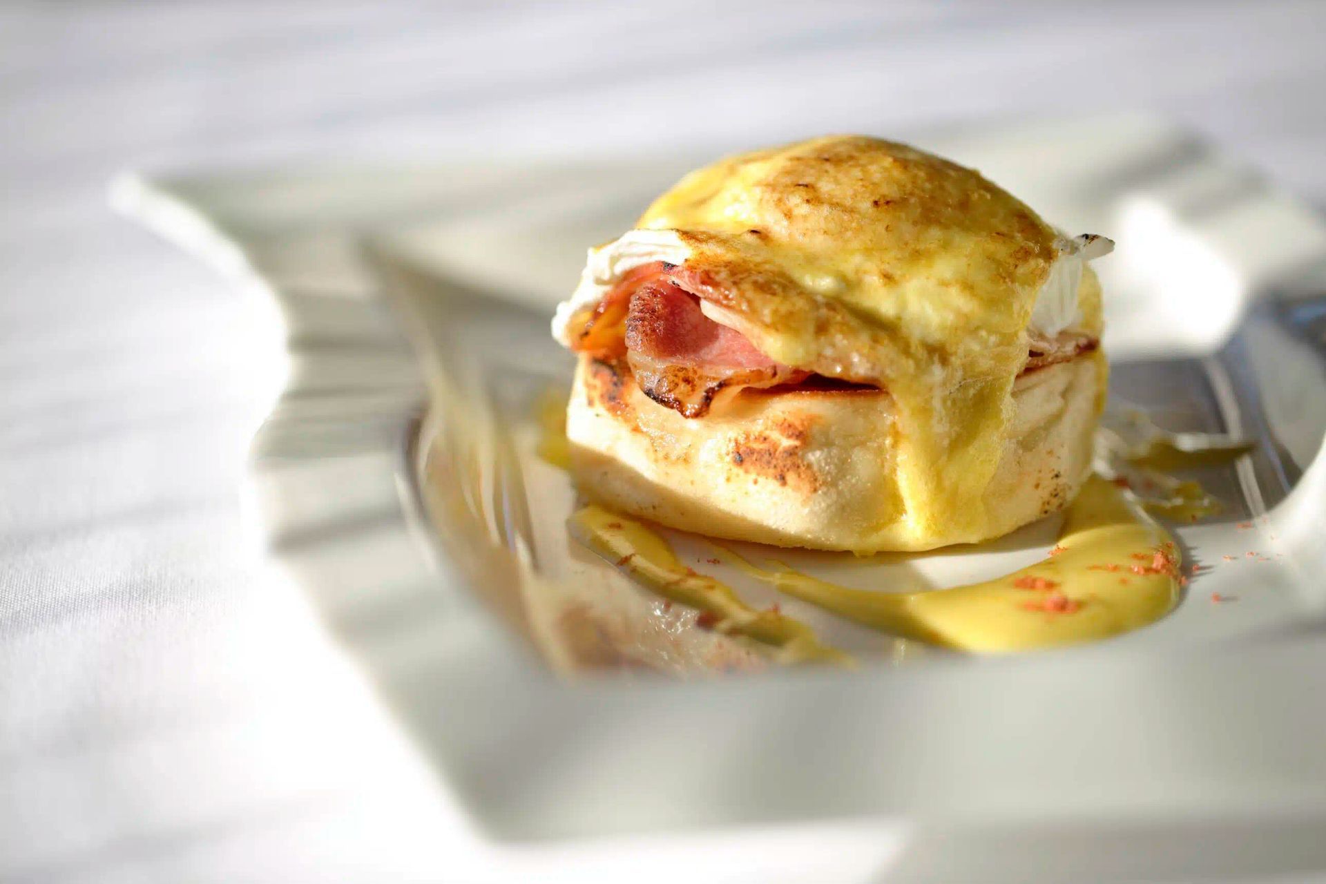 A toasted sandwich on a white plate with melted cheese and a slice of meat