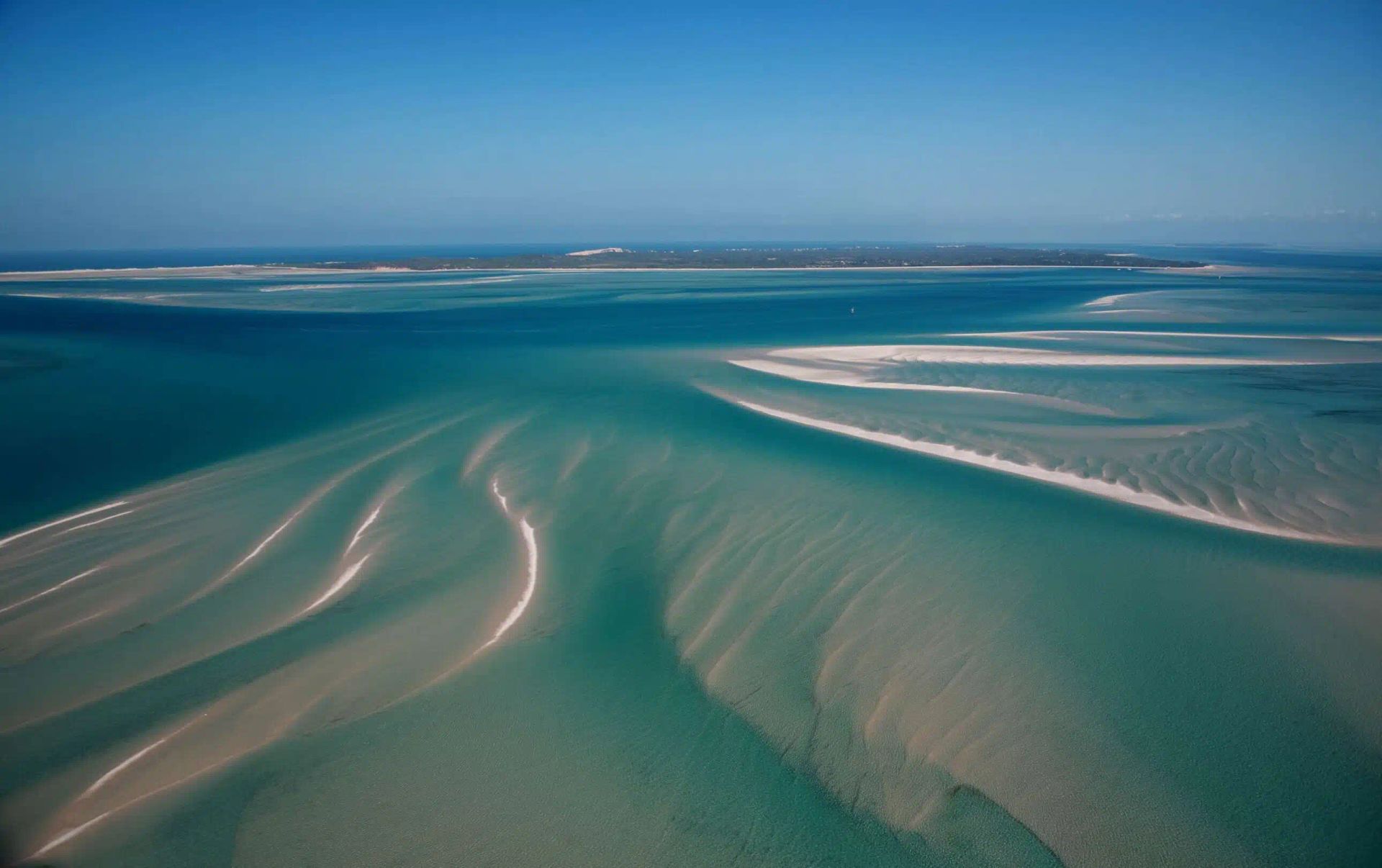Aerial view of turquoise tidal flats and sandbars curving into a blue ocean.