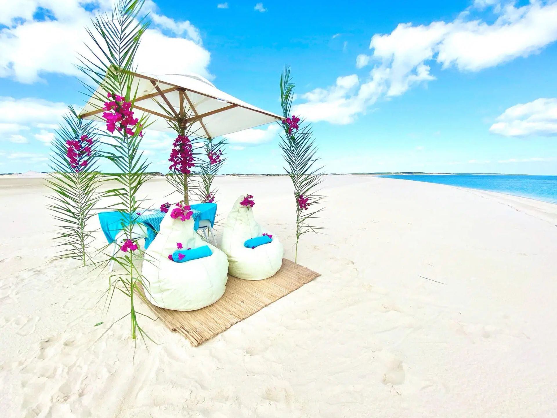 Beach cabana with white cushions and purple flowers on bright white sand by the turquoise sea