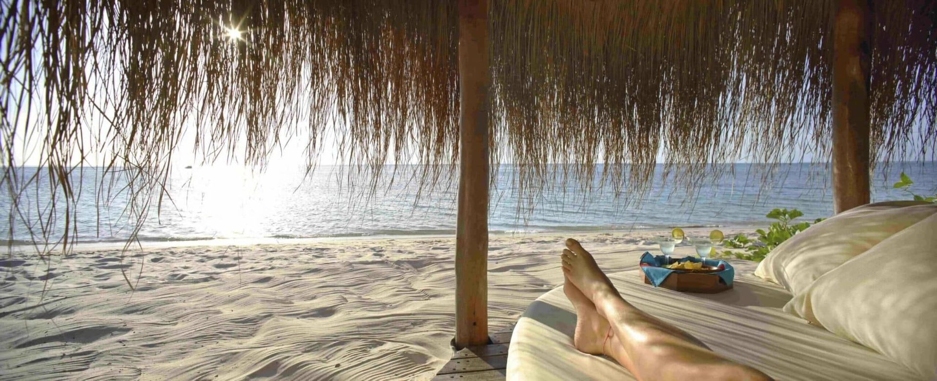 Beachside cabana with a bed, straw roof, and a view of the ocean and sandy shore