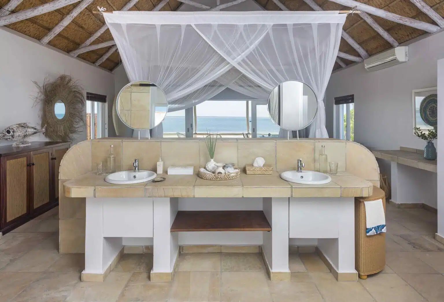 Beachside bathroom with double sinks, round mirrors, and a canopy over the vanity with ocean views