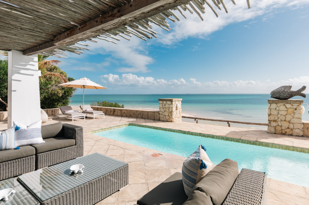 Beachfront patio with wicker lounge chairs and a turquoise pool overlooking the ocean
