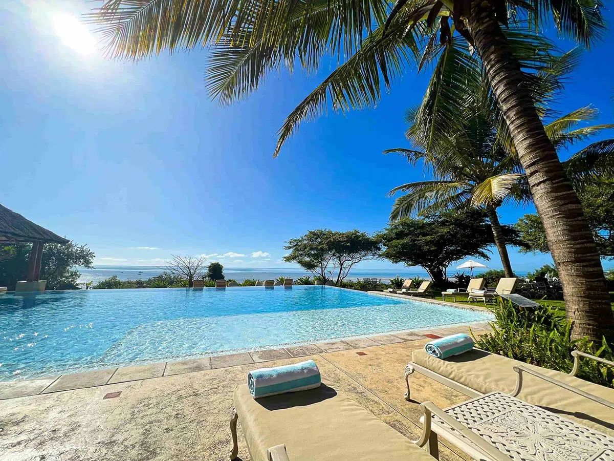 Sunny tropical resort pool beside the ocean with palm trees and lounge chairs