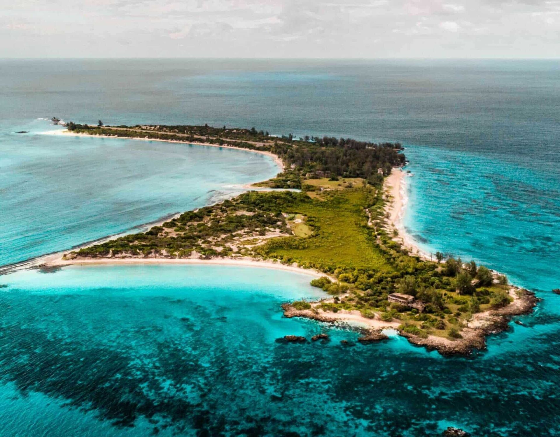 Aerial view of a narrow tropical island with turquoise water and sandy beaches.