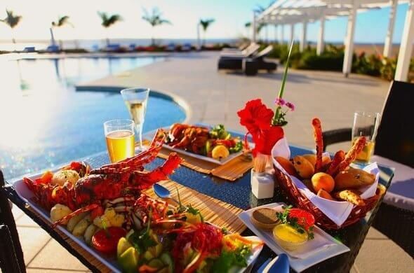 Poolside tropical breakfast spread with fruit, pastries, orange juice, and flowers on a resort patio