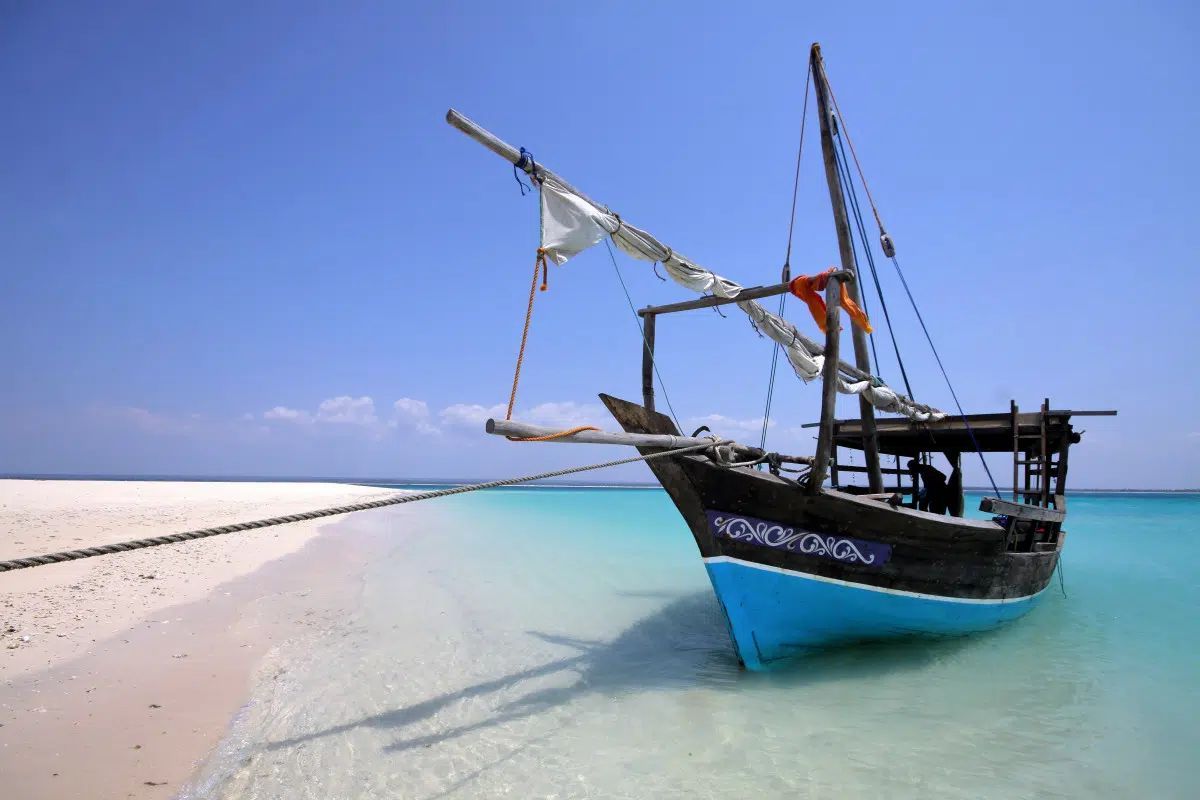 Wooden fishing boat on clear turquoise water beside a white sandy beach under a blue sky