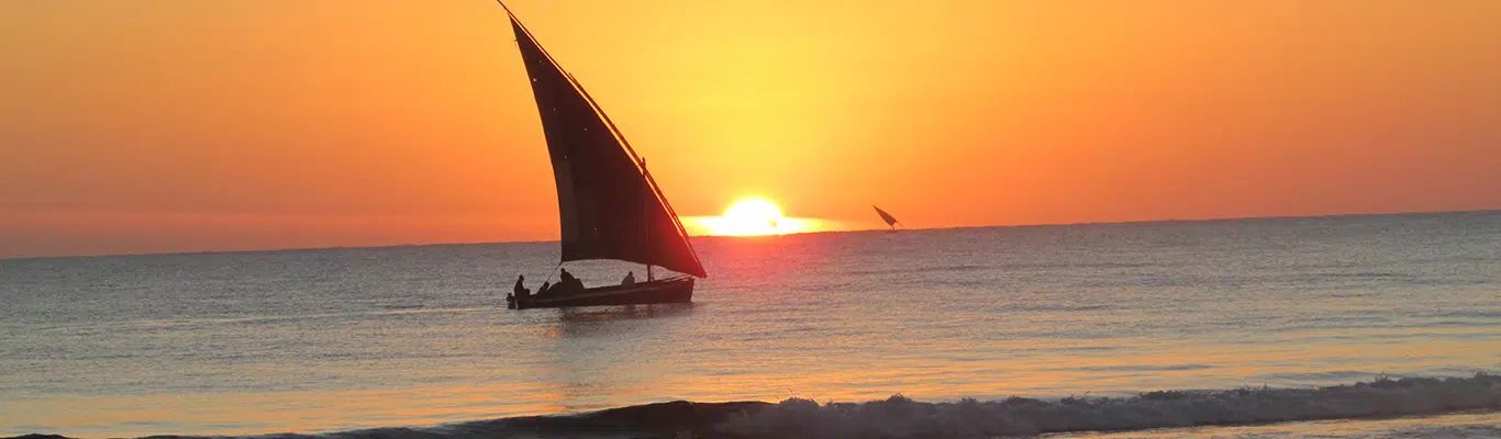 Sailboat silhouetted against a bright orange sunset over calm ocean waves