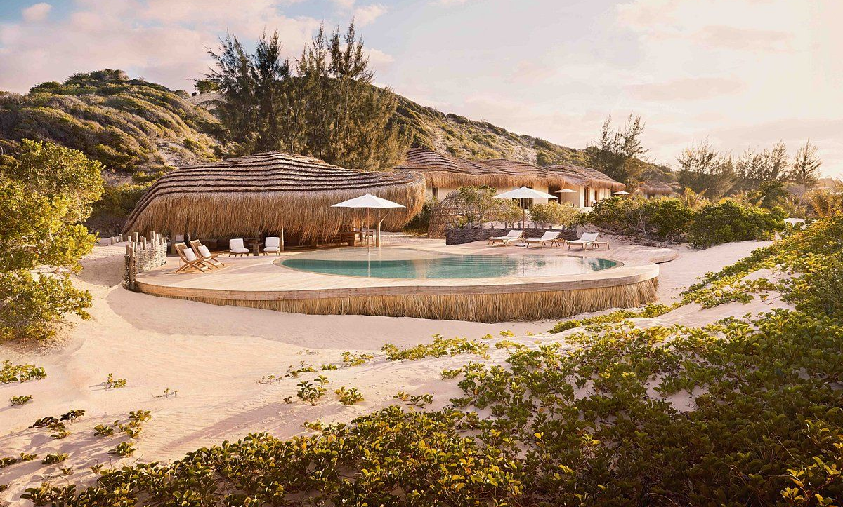 Resort pool with loungers and umbrellas beside a sandy beach and tropical hillside at sunset