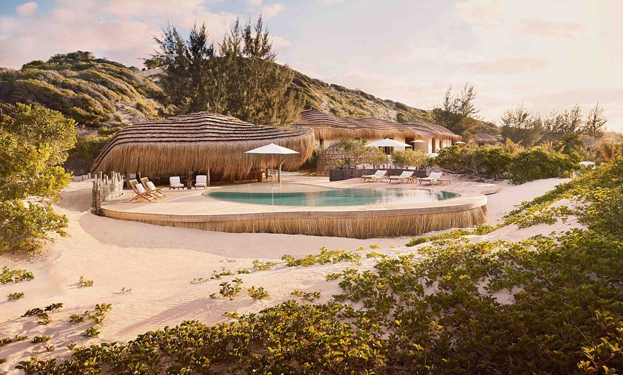 Luxury resort pool in a sandy tropical setting, surrounded by palms and hillside greenery at sunset