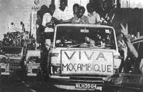 People celebrate on vehicles in Mozambique, with a sign on the front of a truck reading