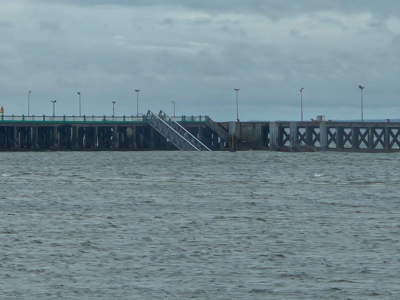 A long pier over choppy water under a cloudy sky, with stairs leading down to the dock.