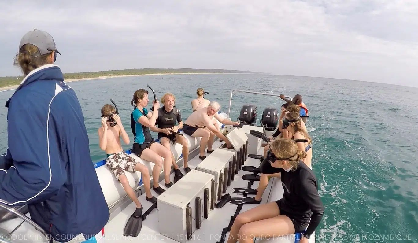 People sitting on the side of a small boat on a sunny ocean trip, with one person steering.
