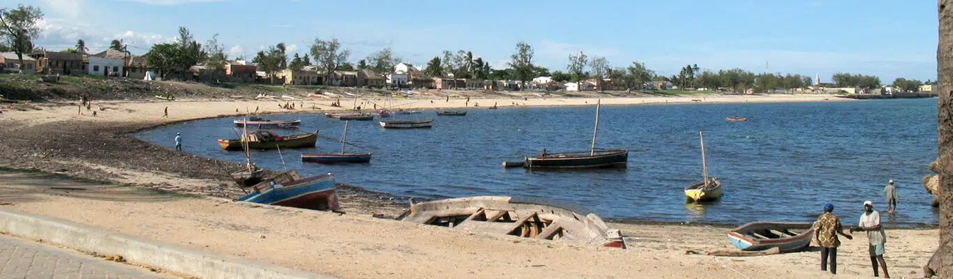 Beach shoreline with small fishing boats floating in calm blue water near a sandy coastal village