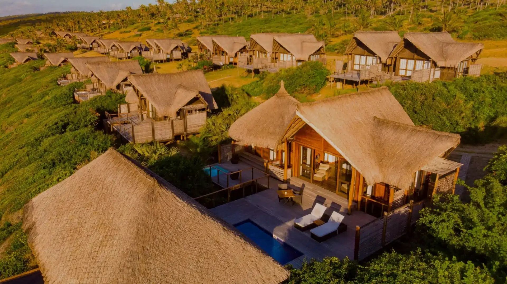 Aerial view of thatched safari lodges in a green landscape at sunset