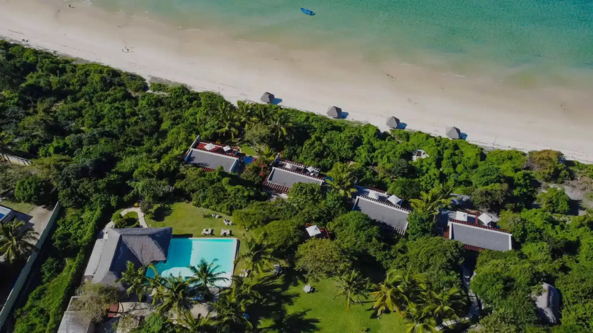 Aerial view of tropical beachfront villas beside a turquoise pool and sandy shore
