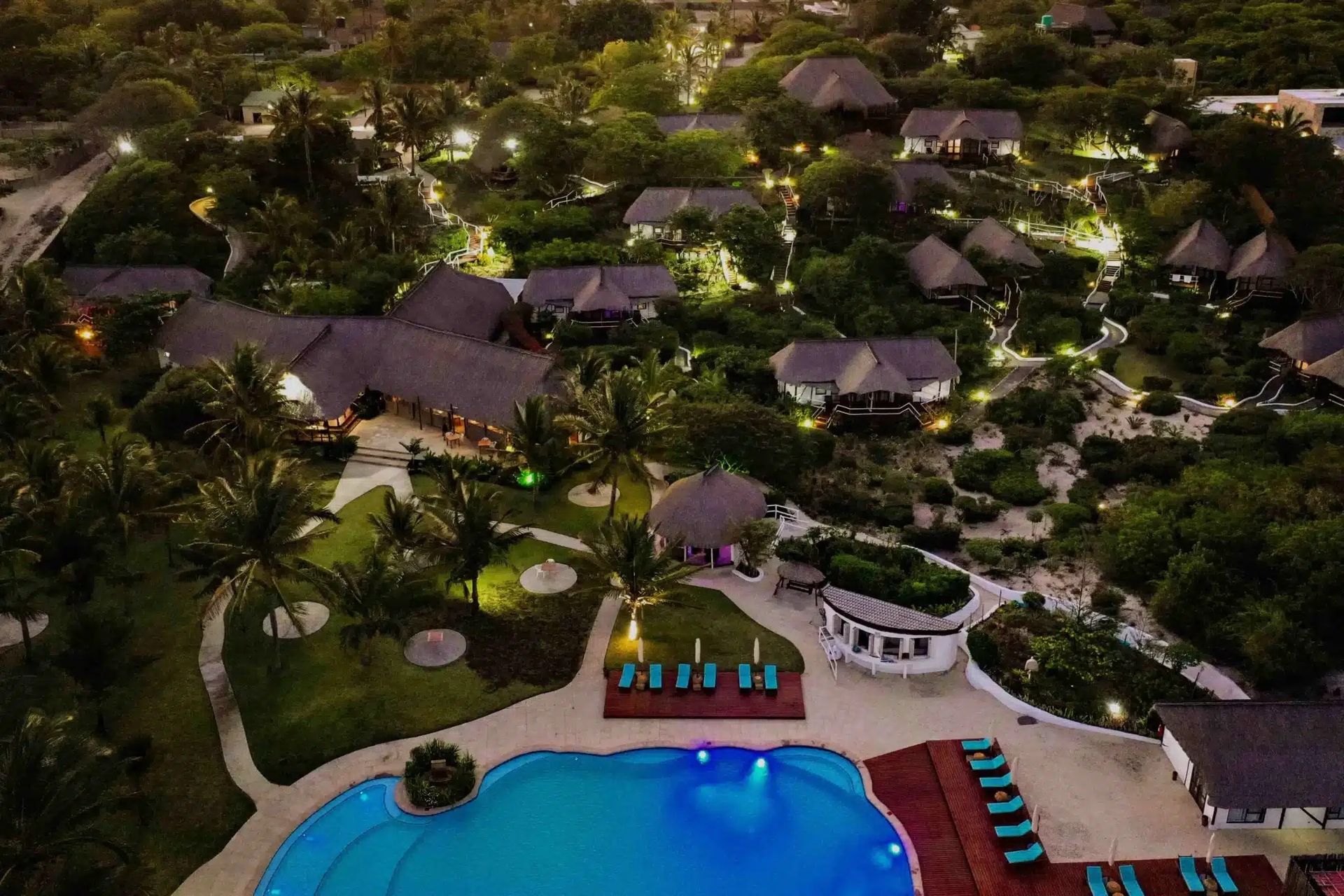 Aerial view of a tropical resort with thatched villas, lush greenery, and a pool by the beach