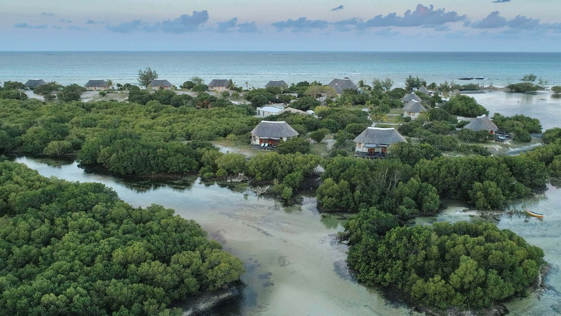 Aerial view of a lush coastal island with mangroves, shallow water, and small houses near the shore