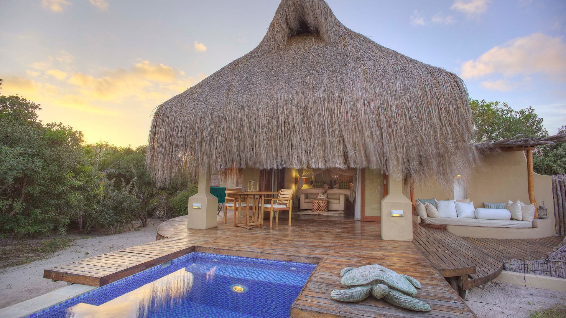Thatched beach hut with a pool at sunset, surrounded by tropical greenery