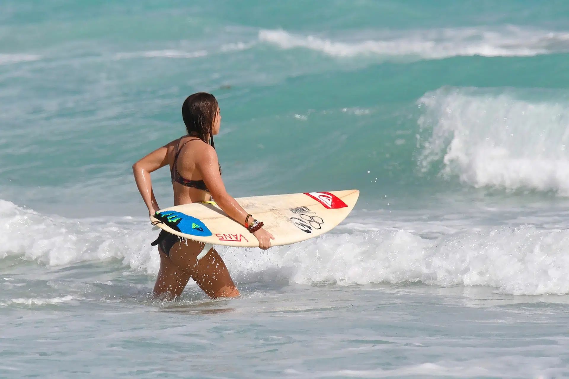 Person carrying a surfboard in shallow ocean water near breaking waves