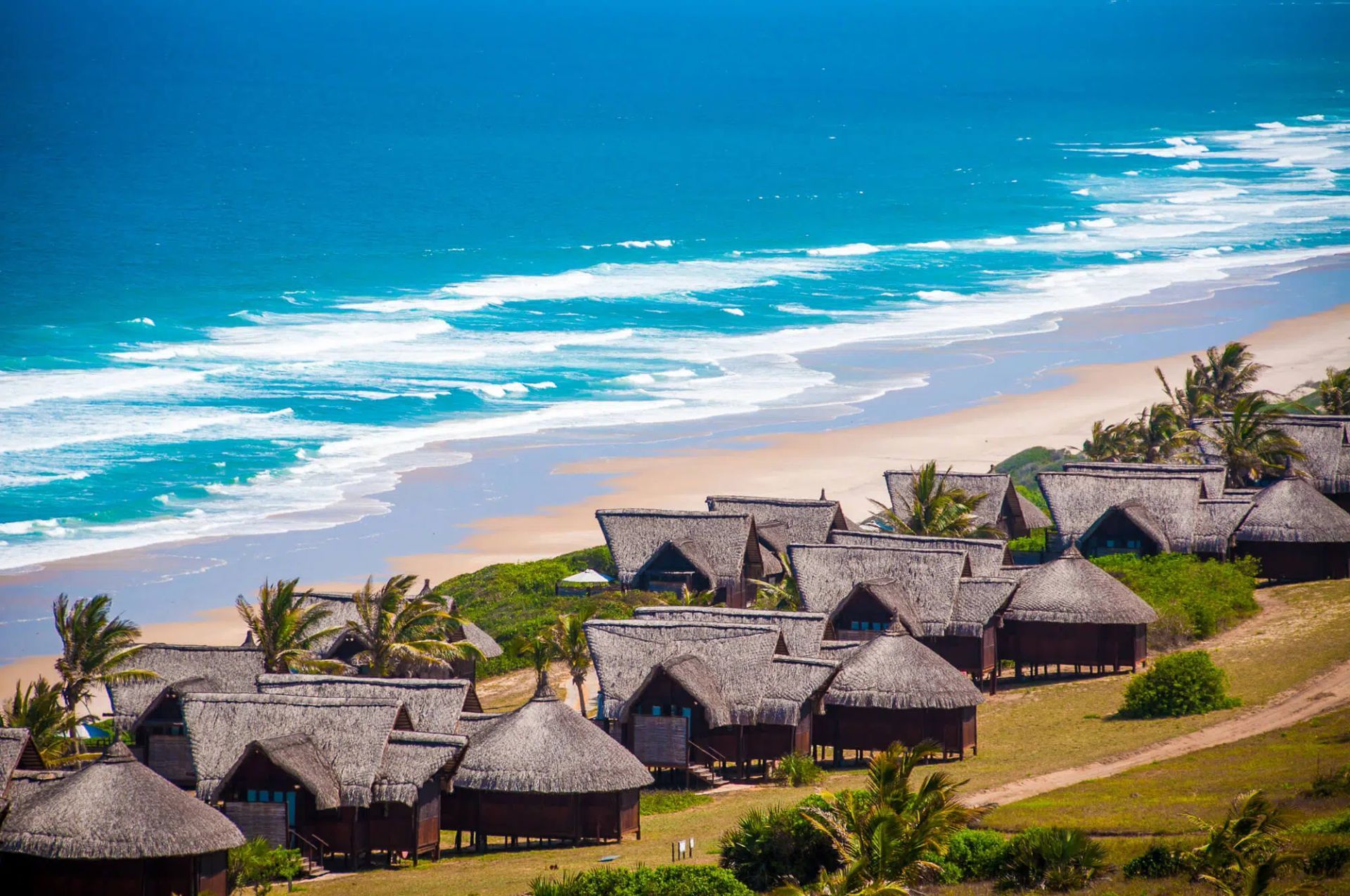 Thatched beach resort cabins above turquoise ocean and sandy shore