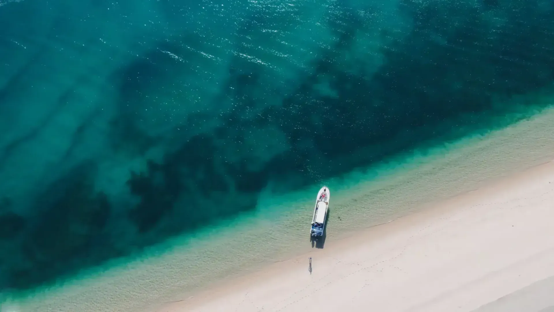 Aerial view of a boat on a pale sandy beach beside clear turquoise water.