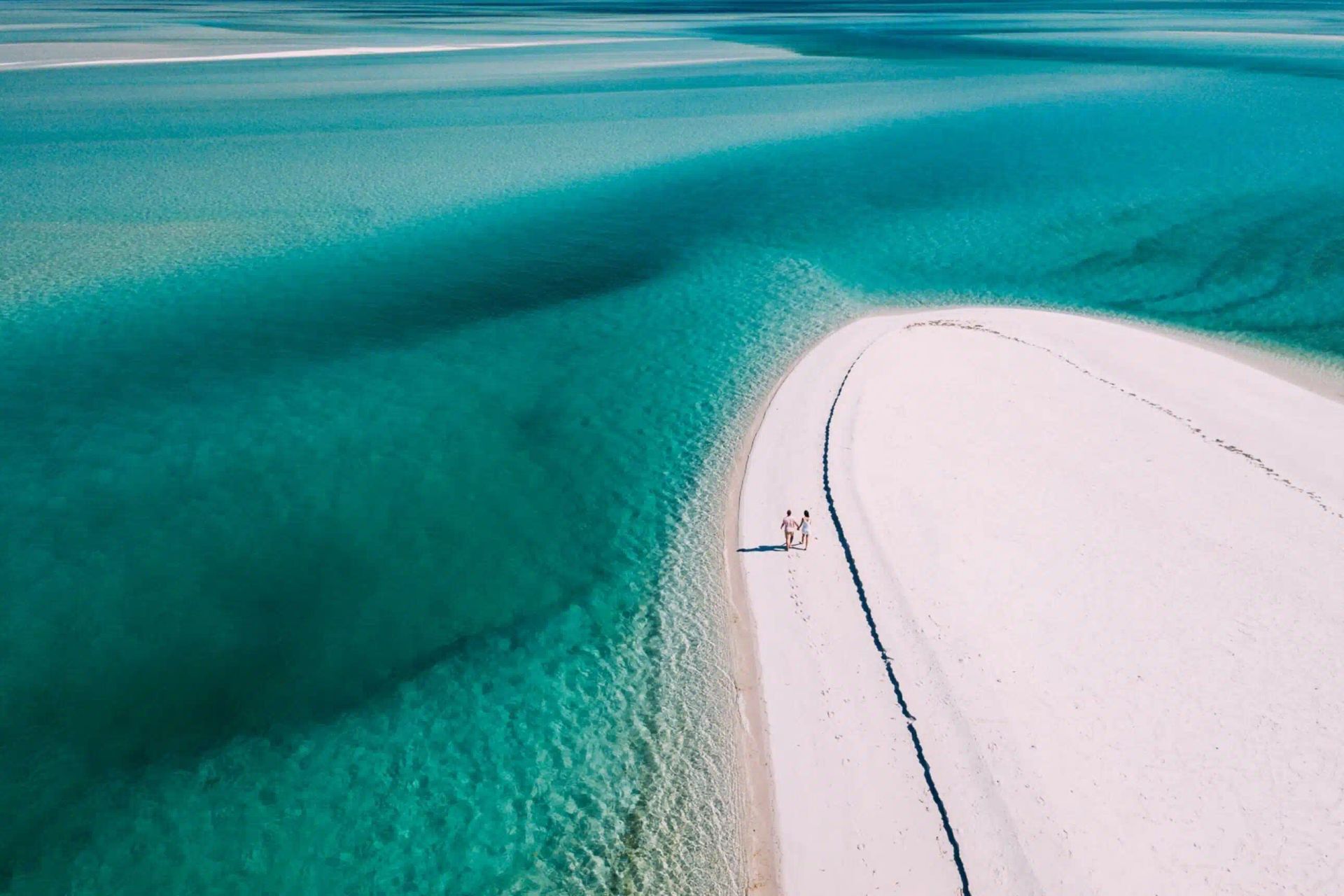 Aerial view of a white sandbar beside turquoise water with a small dock or walkway
