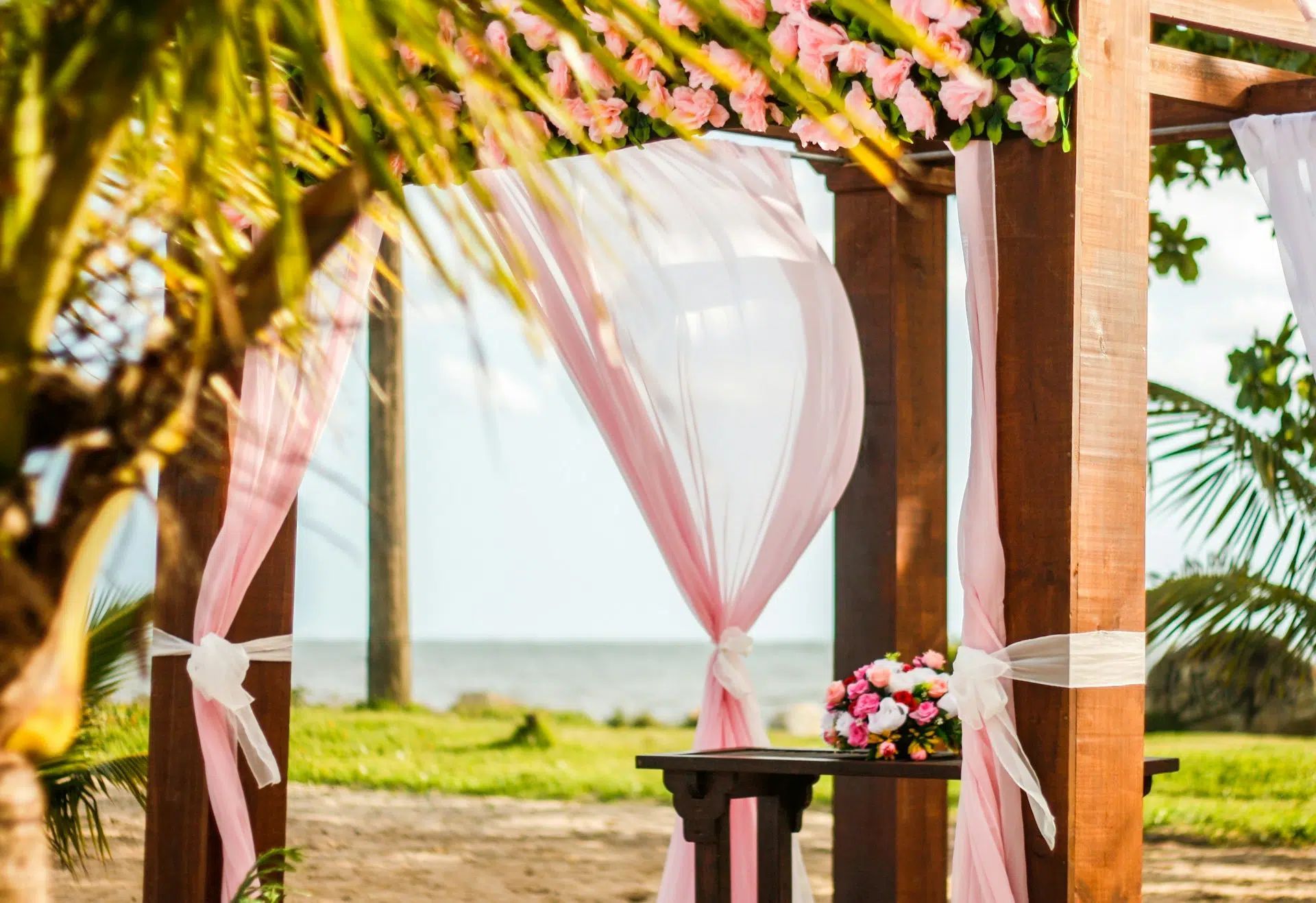 Decorated seaside wedding pavilion with pink drapes, flowers, and ocean view