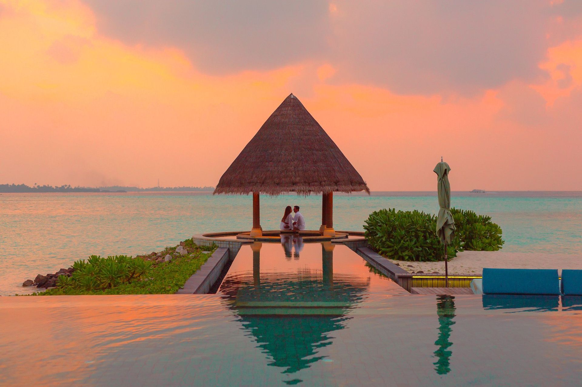 Couple seated on a dock at sunset beside an infinity pool overlooking the ocean