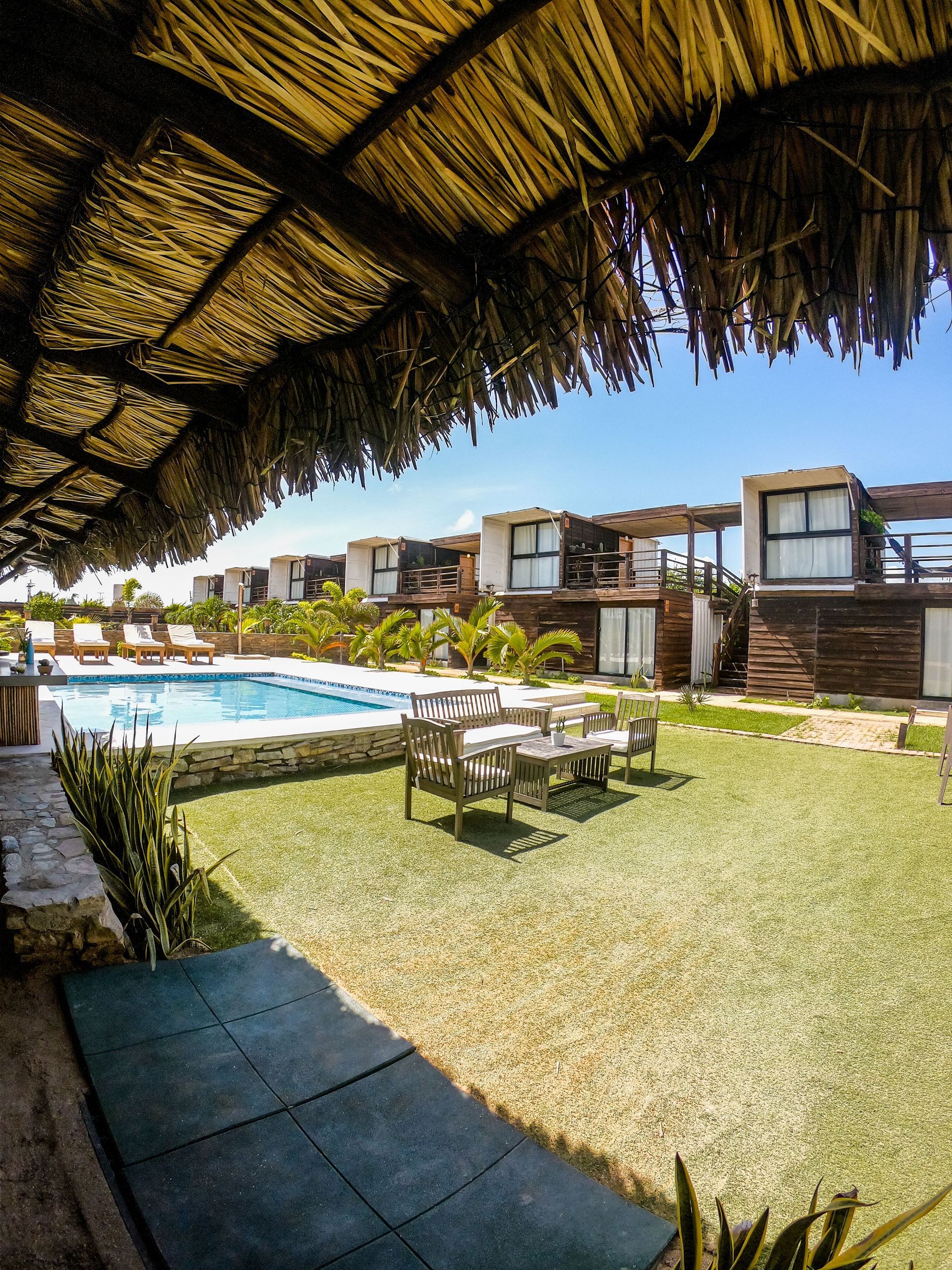 Resort poolside patio with thatched shade roof, lounge chairs, and modern cabanas by the water