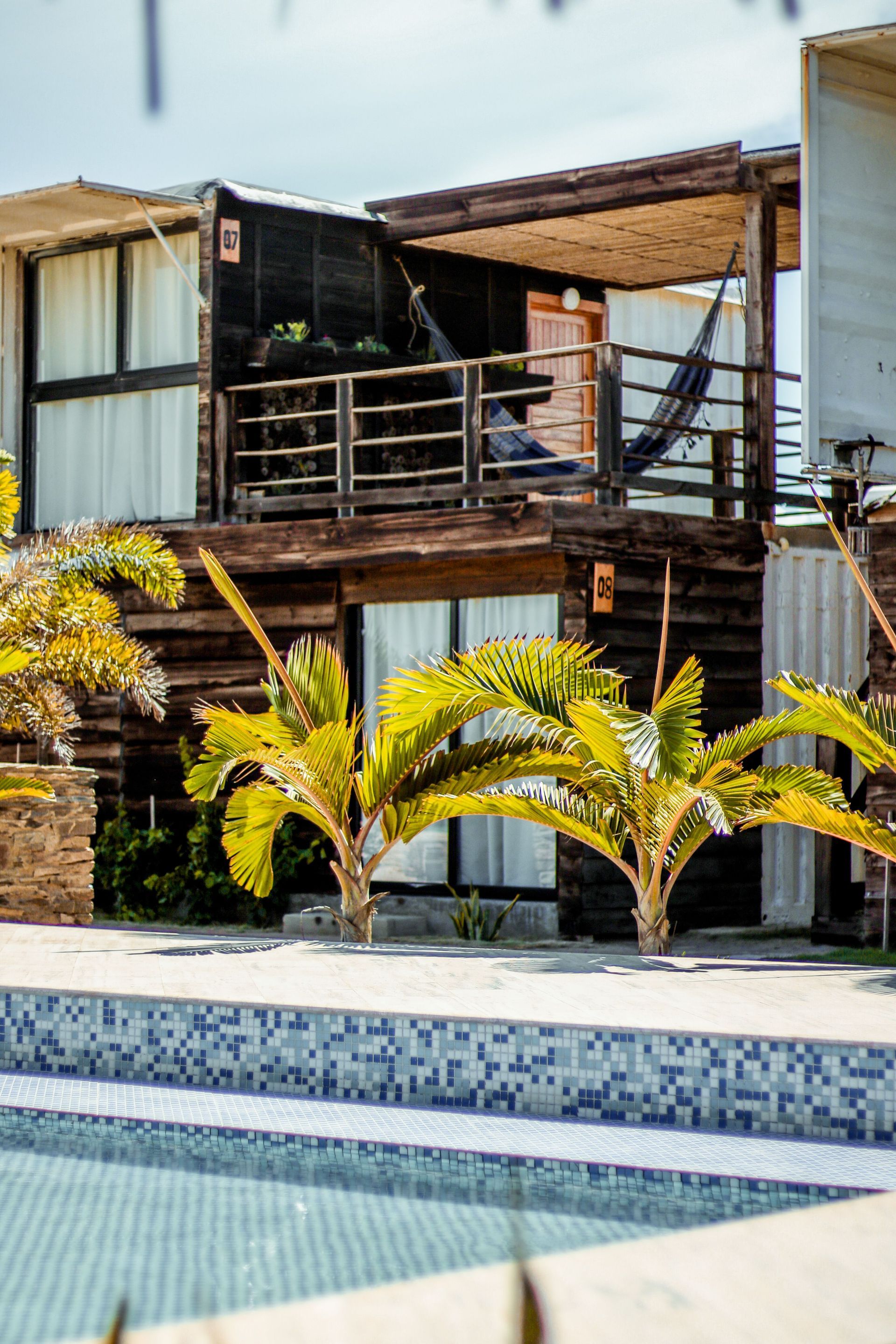 Modern house with wooden balconies and yellow palms beside a tiled pool