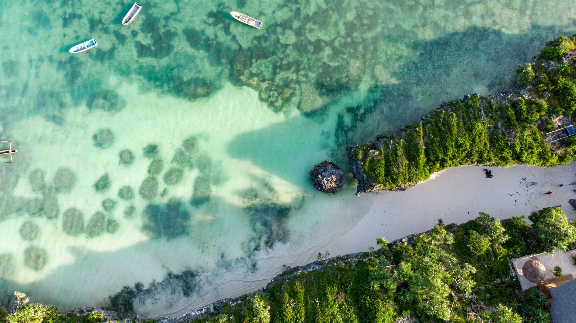 Aerial view of a turquoise tropical beach with boats, sandbar, and lush green shoreline