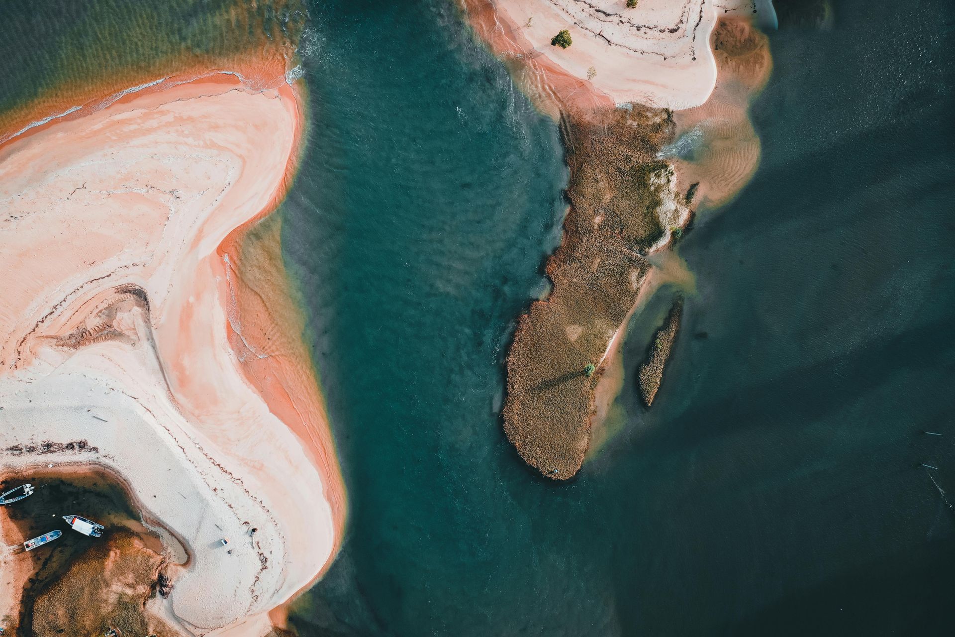 Aerial view of a rocky island in dark blue water beside swirling white and peach sandbars.