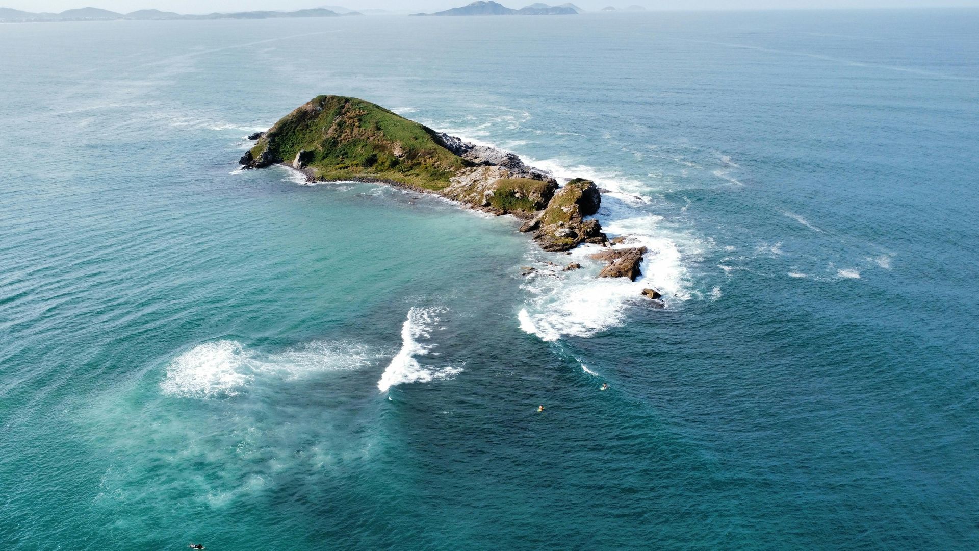 A small rocky green island in turquoise ocean with waves crashing around it