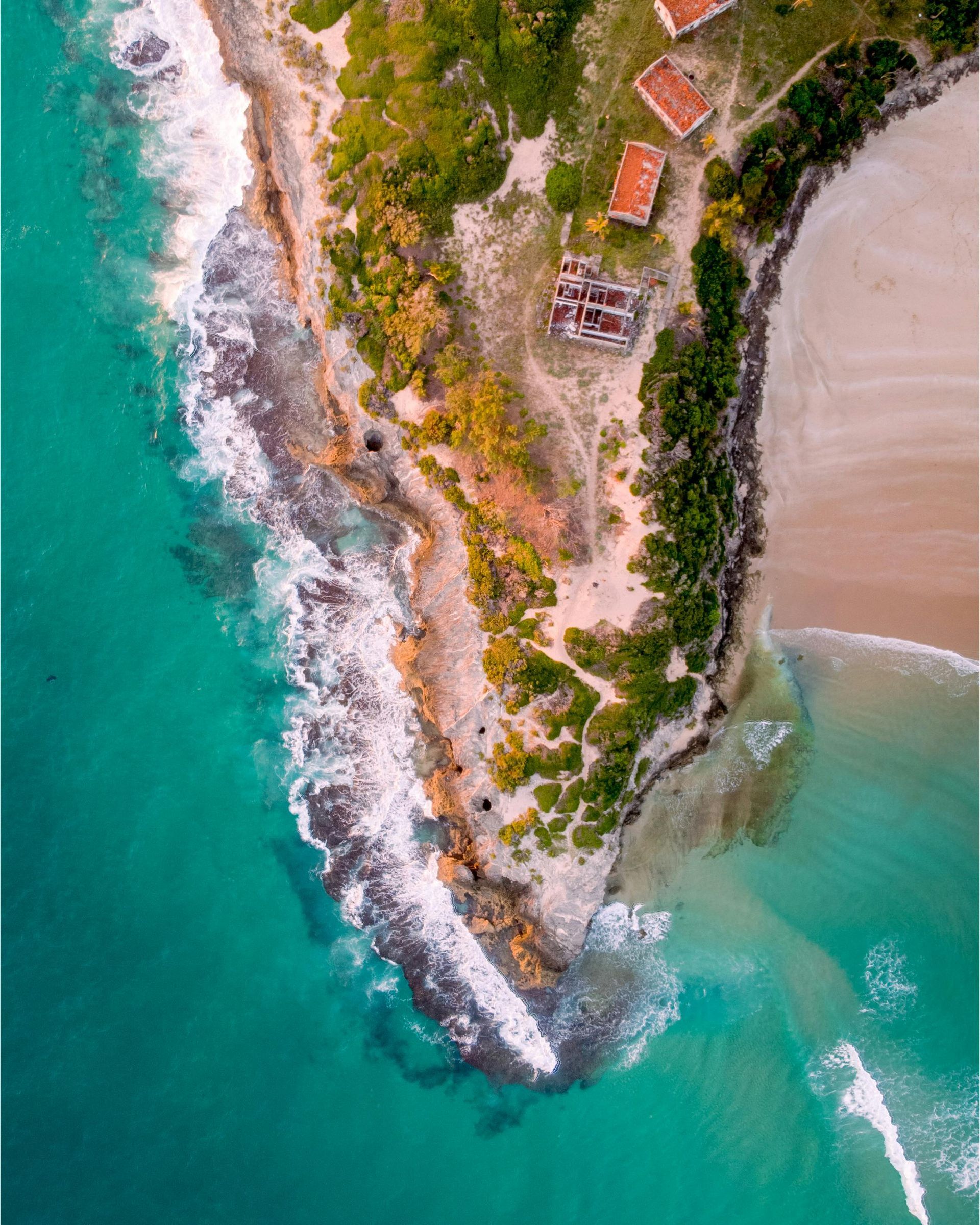 Aerial view of a rocky tropical point with turquoise water, white surf, and a sandy beach cove.