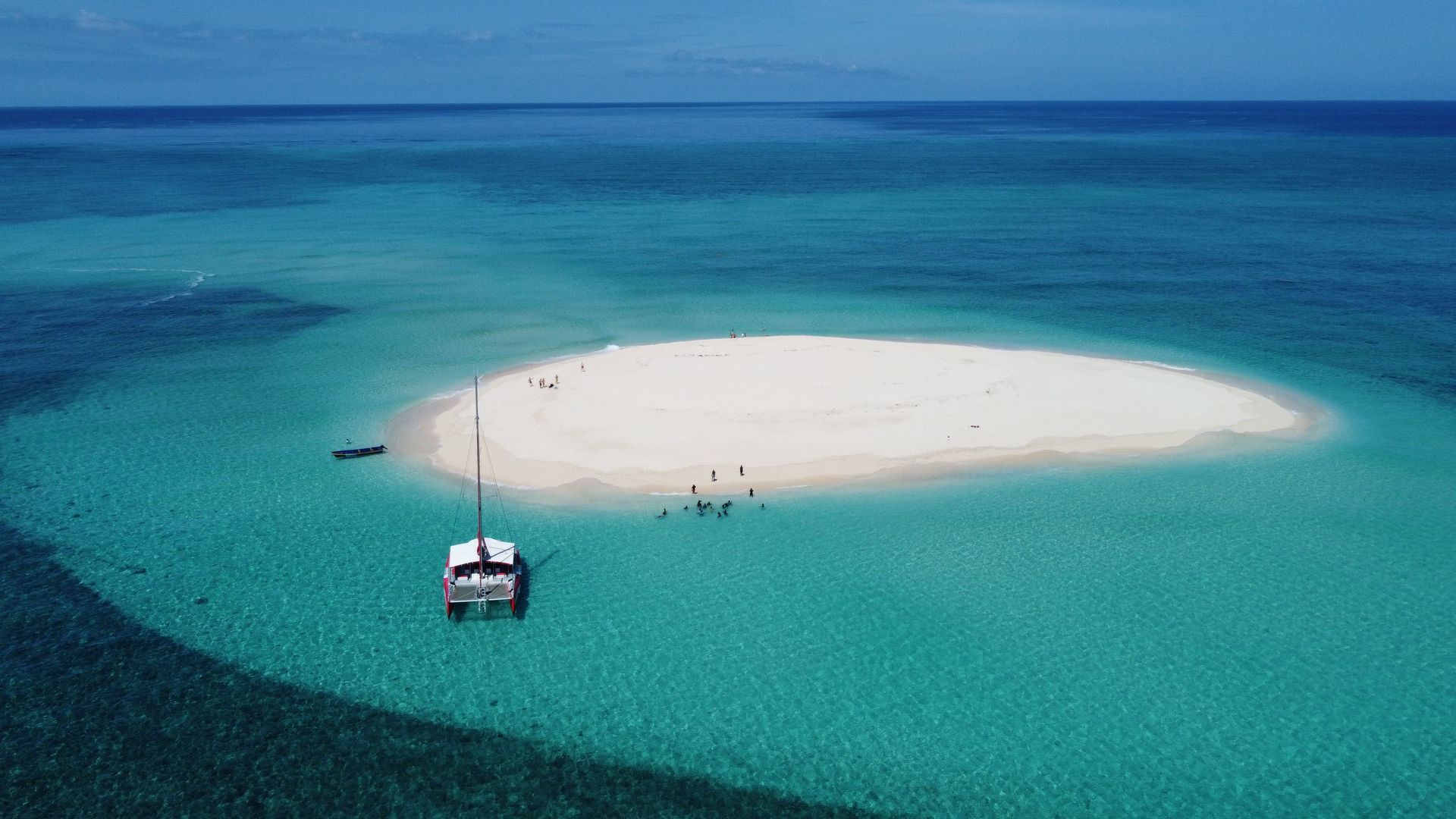A small boat near a white sand island surrounded by turquoise and deep blue ocean.