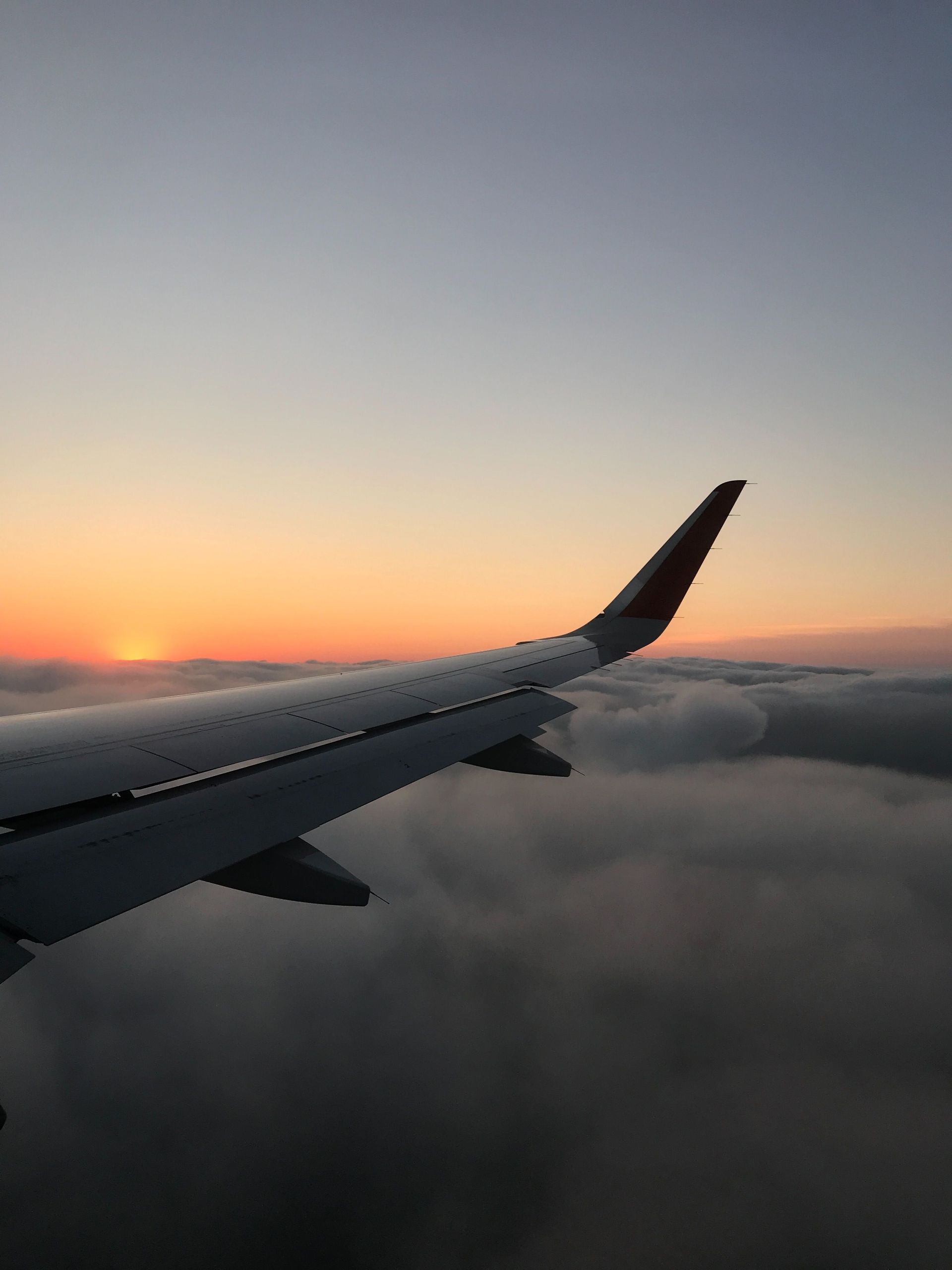 Airplane wing above clouds at sunset with orange and blue sky