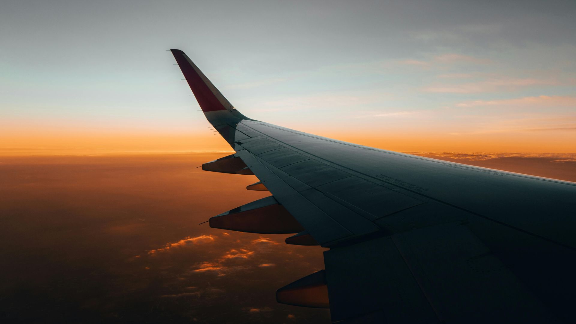 Airplane wing at sunset above clouds, with orange and blue sky on the horizon