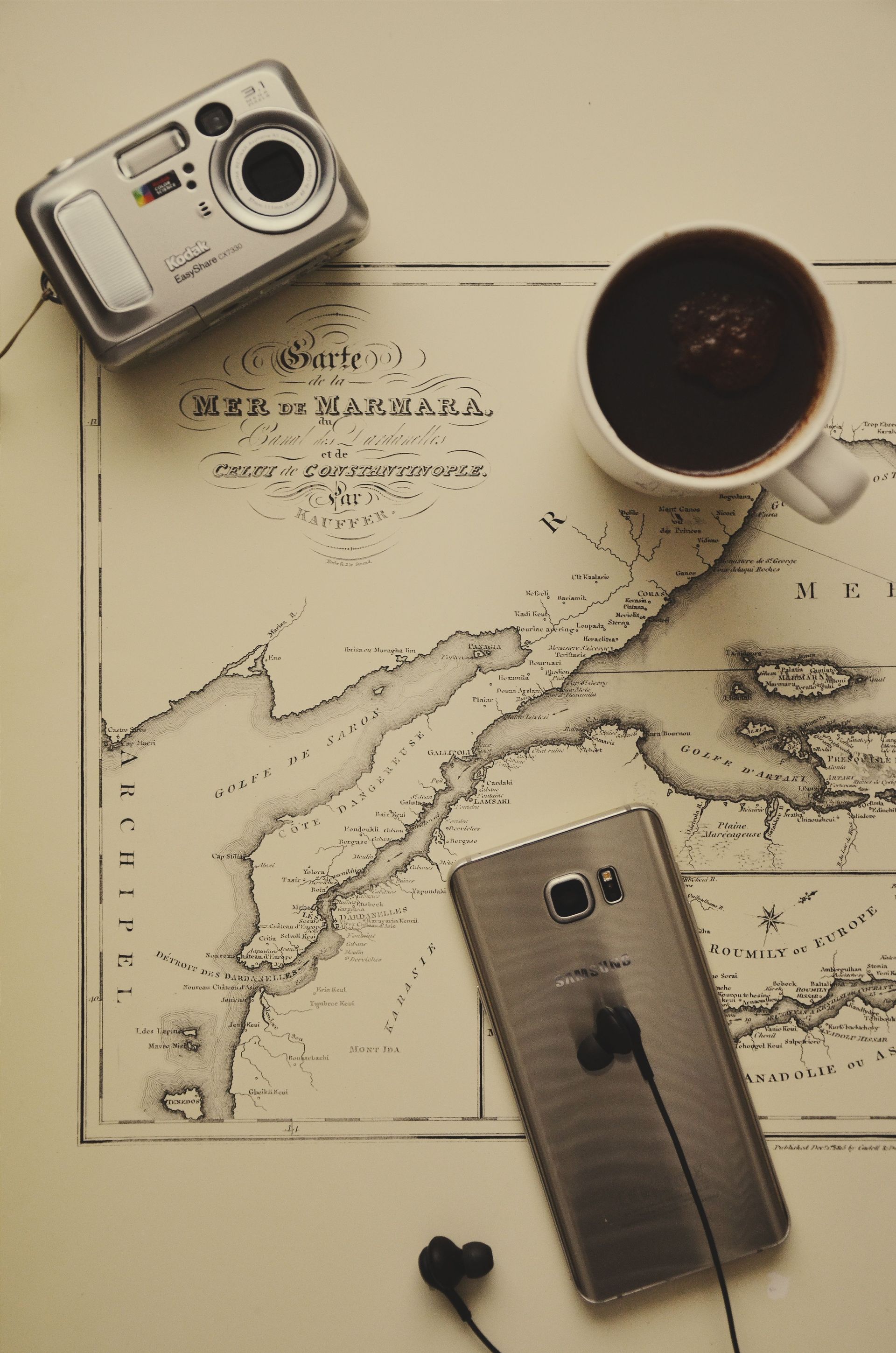 Travel flat lay with a vintage camera, coffee cup, smartphone, earbuds, and a map on a beige table