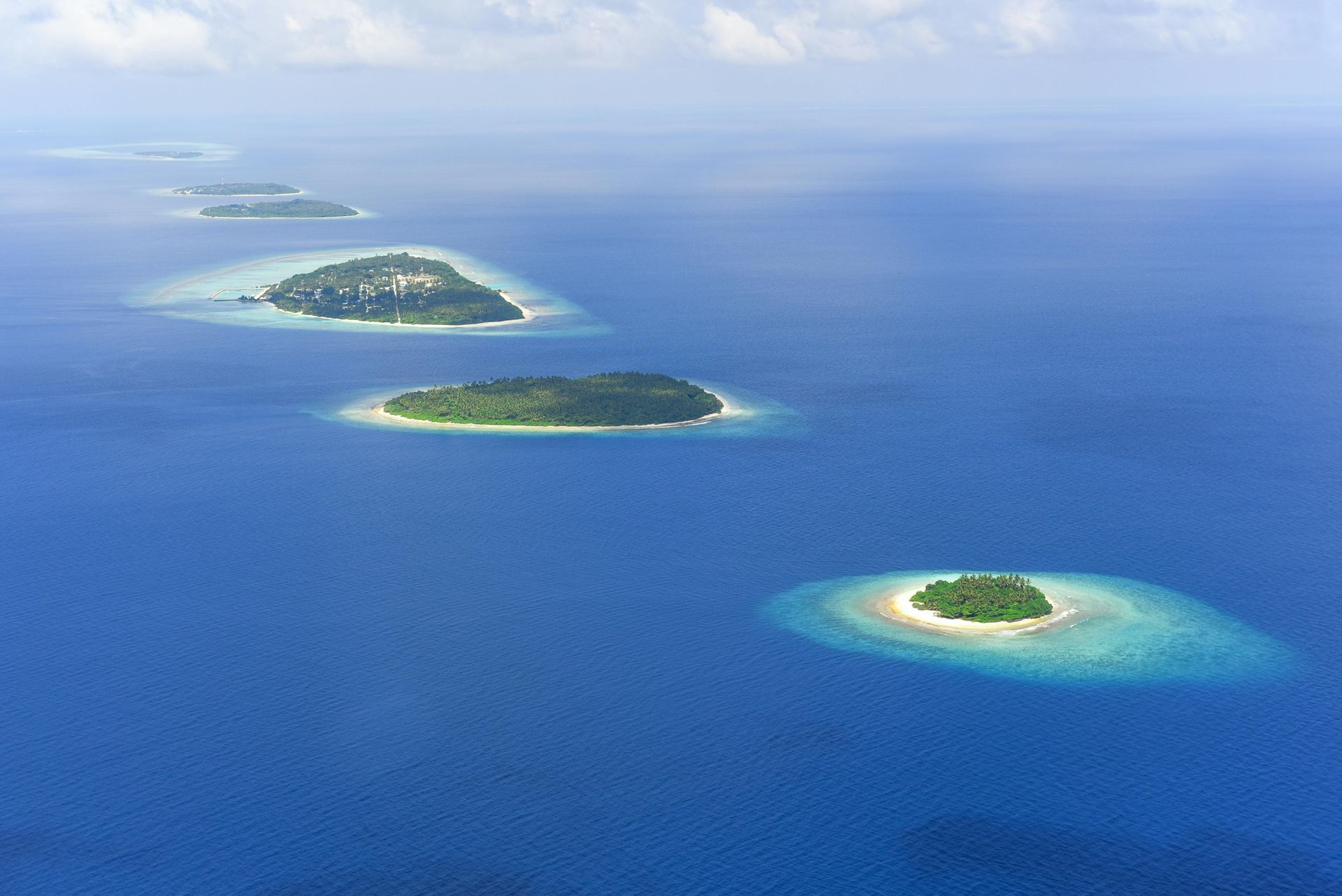 Aerial view of three small green islands in deep blue ocean with turquoise shallows