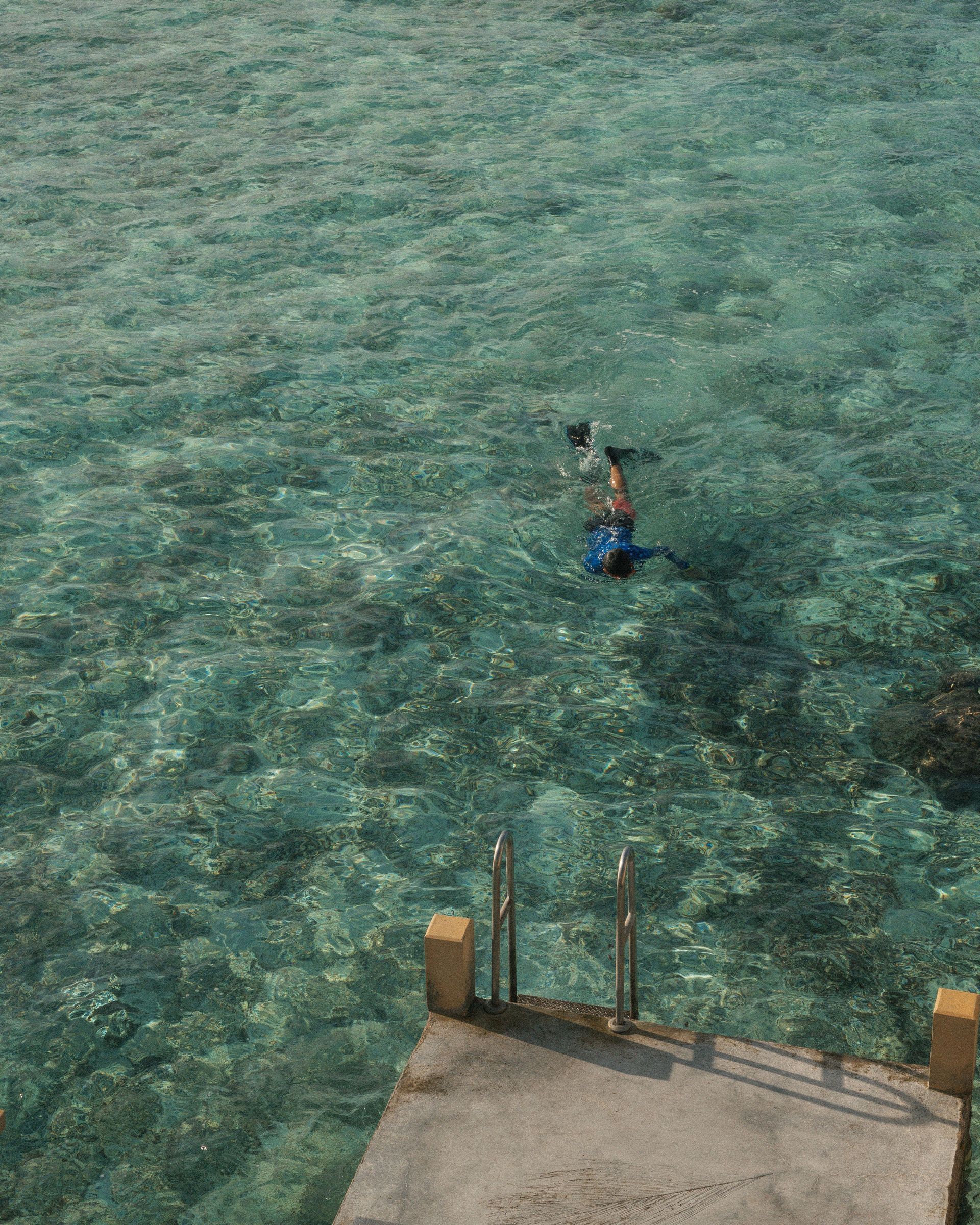 Person swimming in clear turquoise water near a dock at the bottom of the frame.