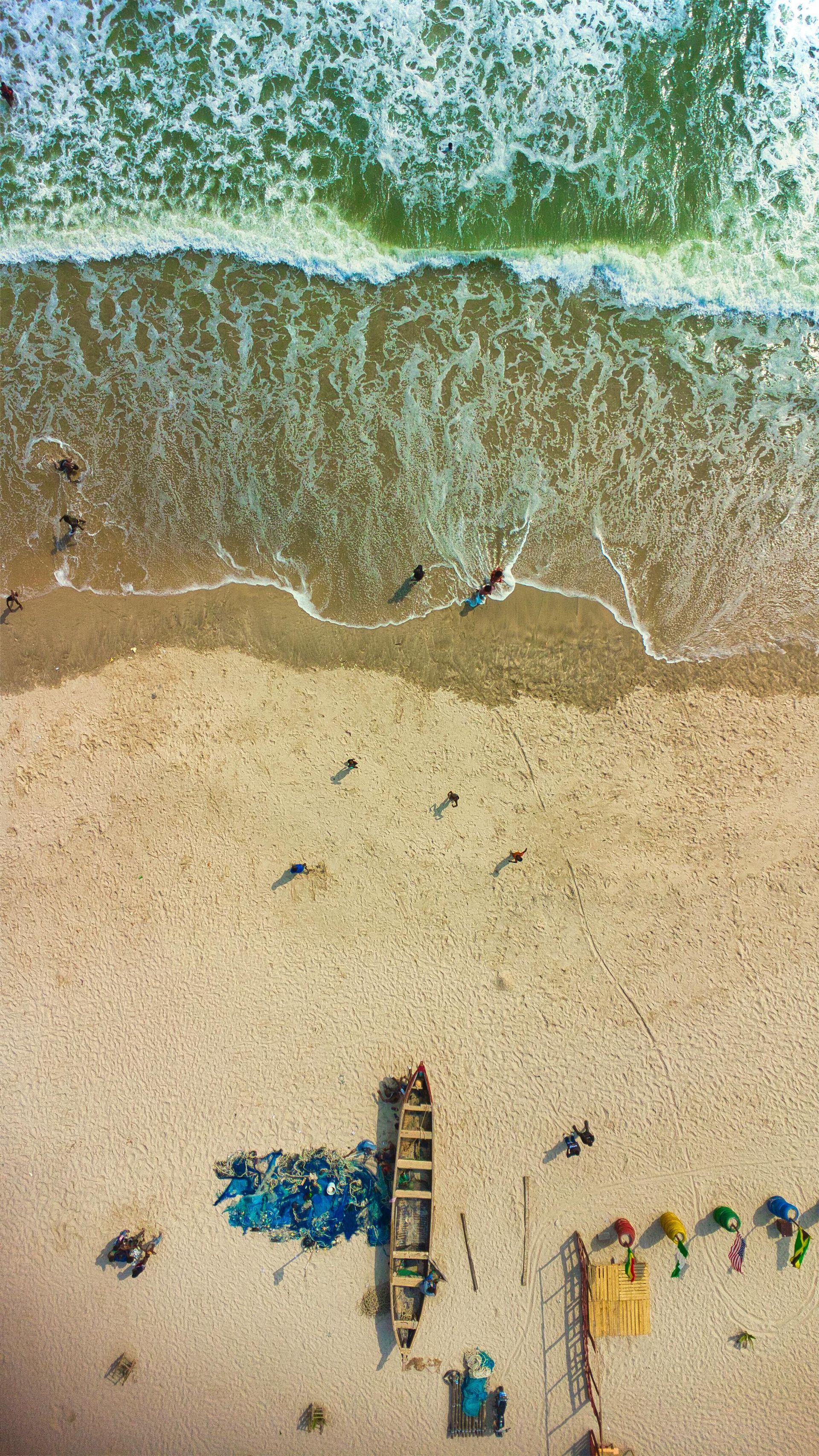 Aerial view of a sandy beach with waves, umbrellas, lounge chairs, and a lifeguard tower.
