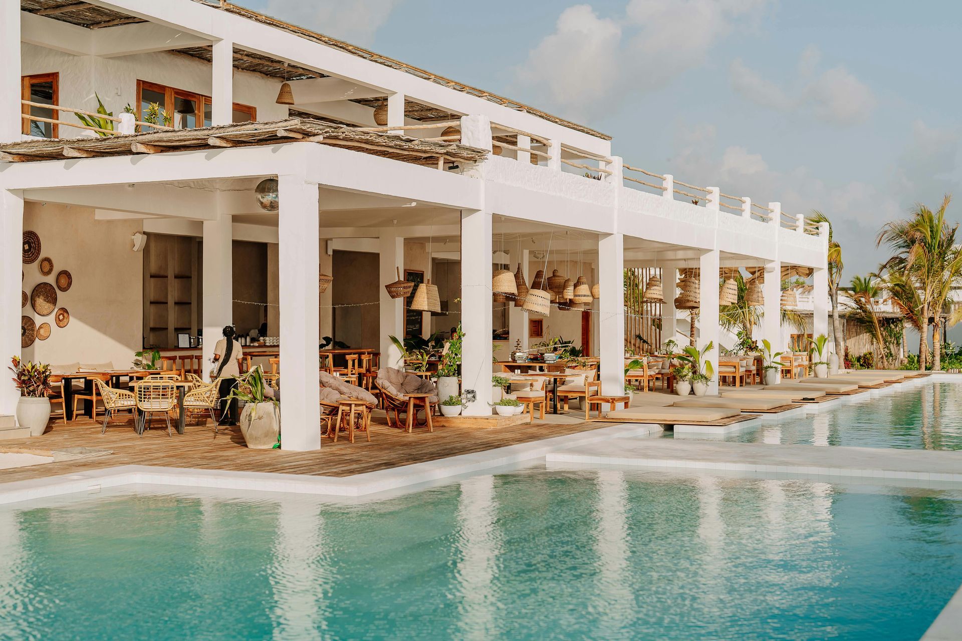 White beachfront resort with open-air terrace beside a turquoise infinity pool