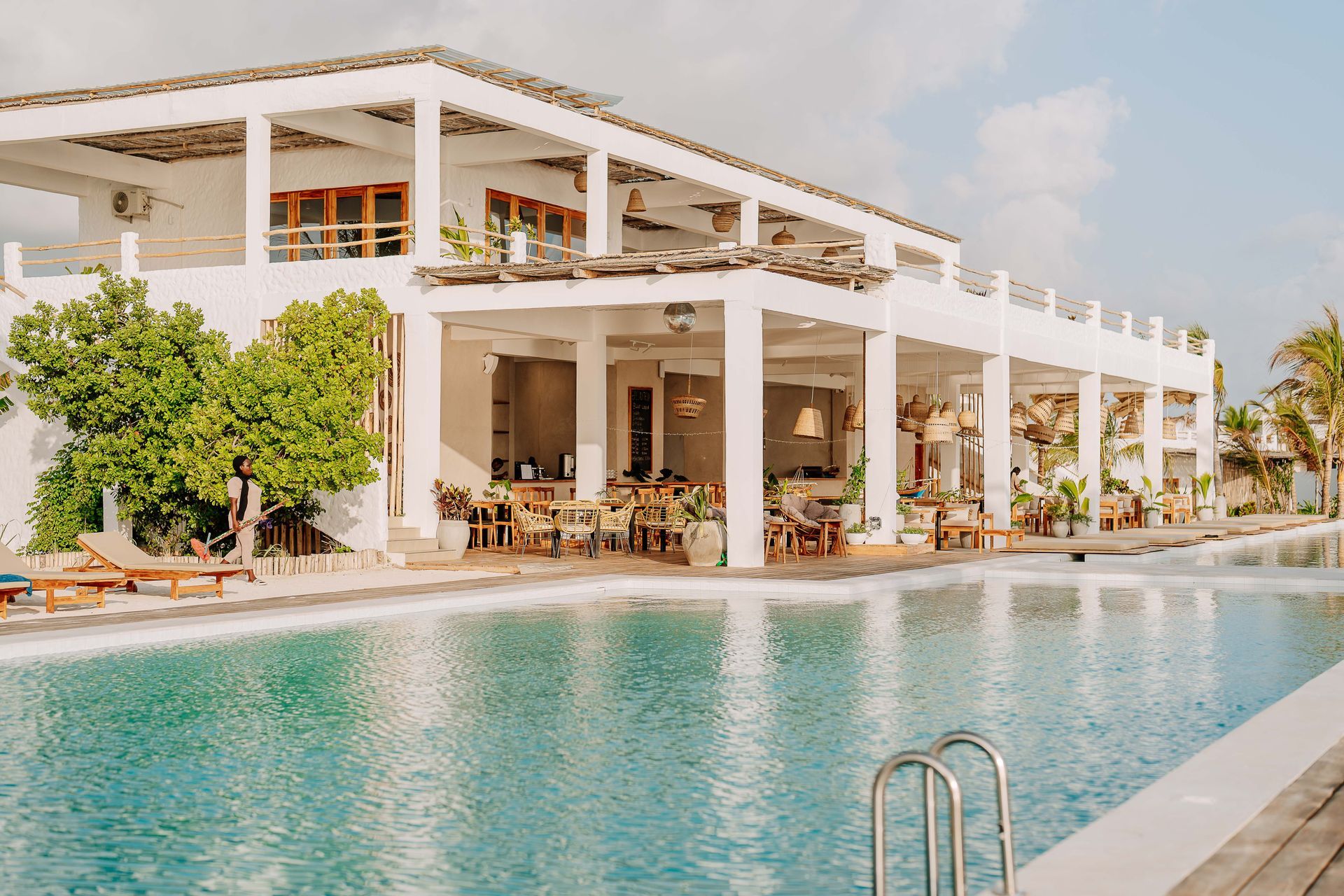 Modern white resort with a turquoise pool and open-air dining terrace by the water