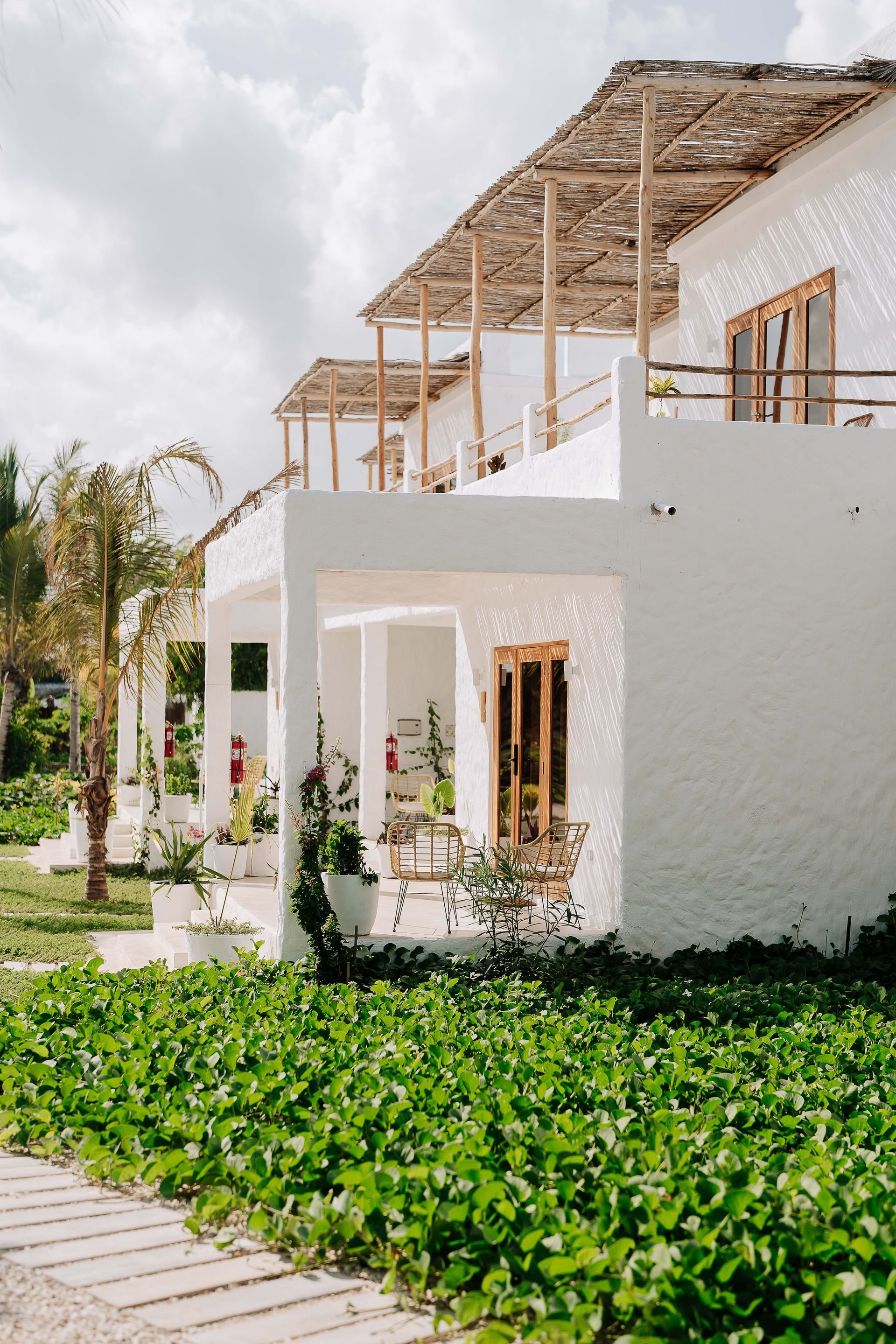 White villa with open wooden roof beams and green garden vines in the foreground
