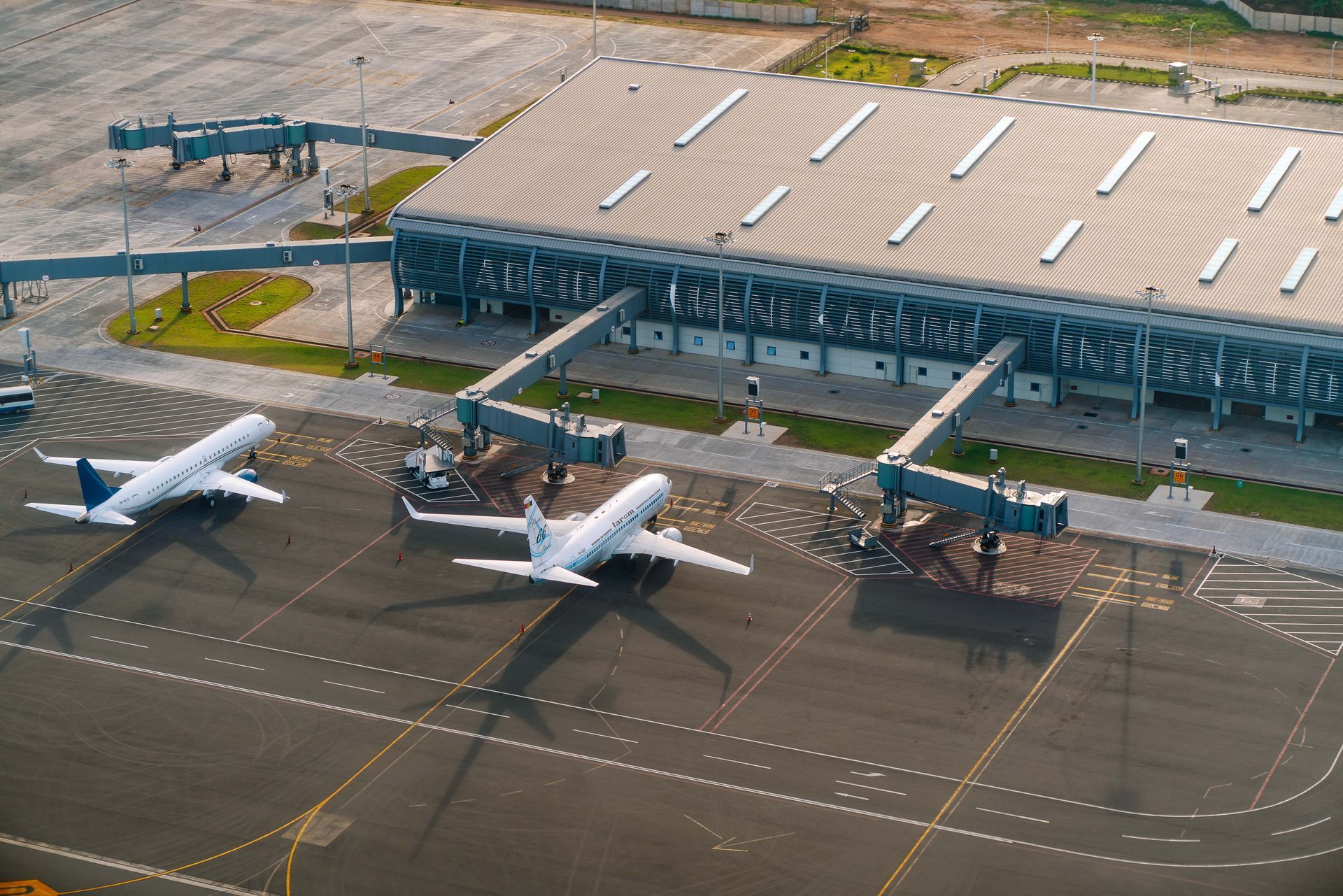 Two white airplanes parked at an airport gate beside a teal terminal building