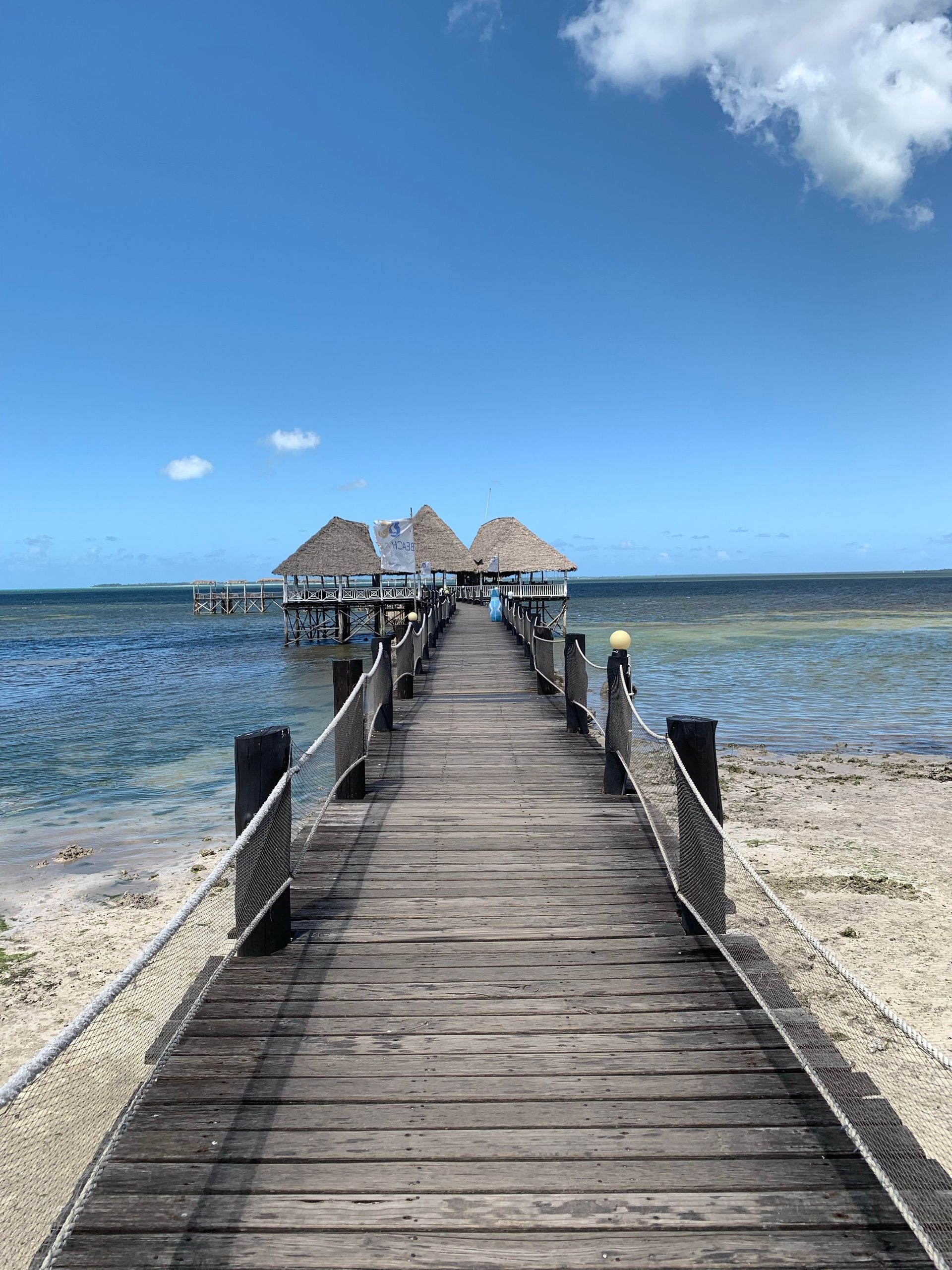 Wooden pier leading to thatched huts over clear blue water under a bright sky