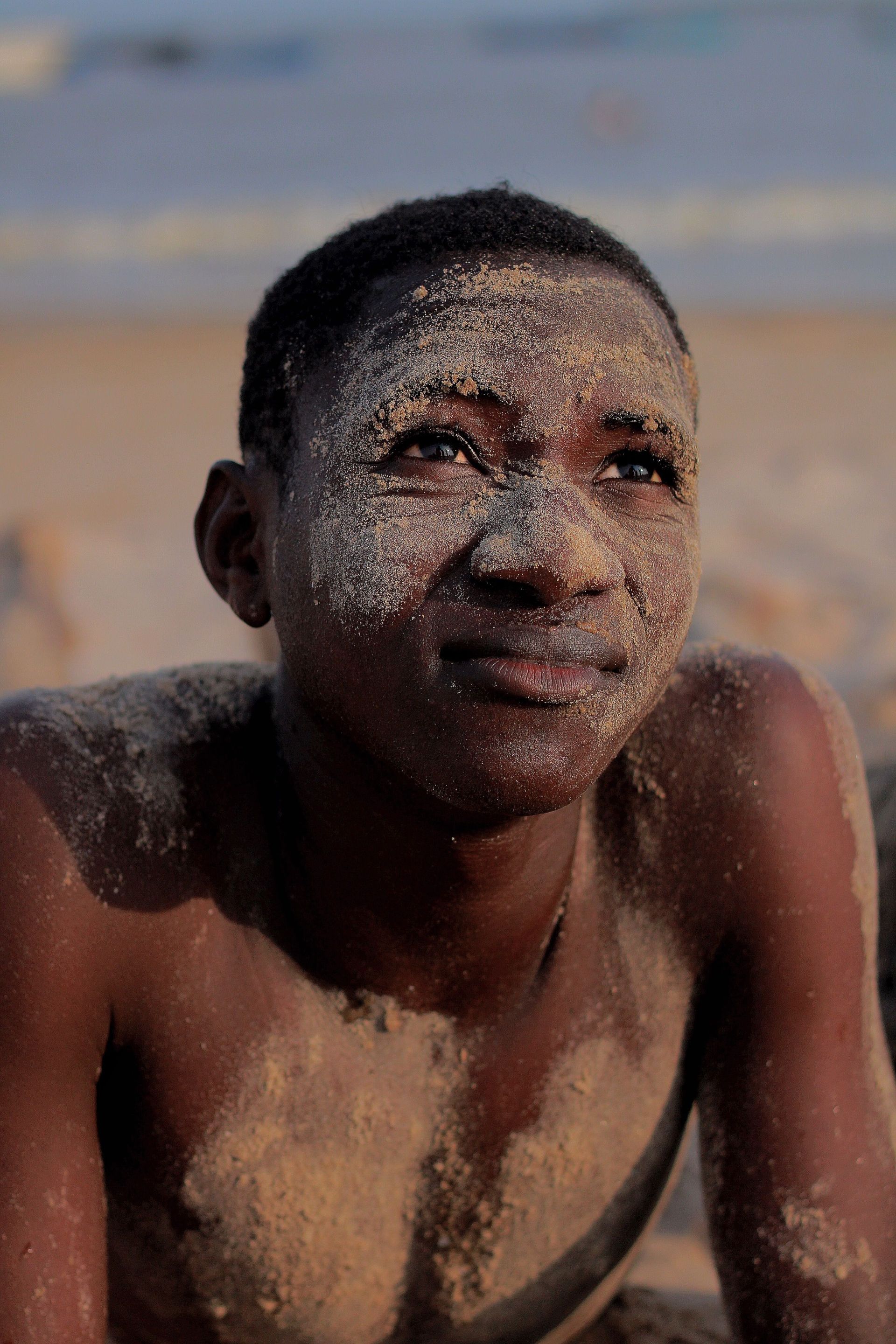 A wet person on a beach, lying on the sand and looking off to the side.