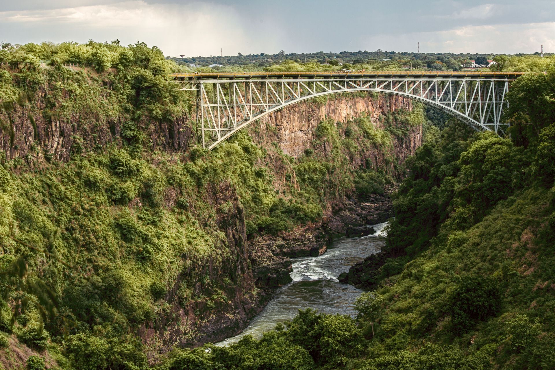 Green canyon with a tall steel arch bridge spanning a river below