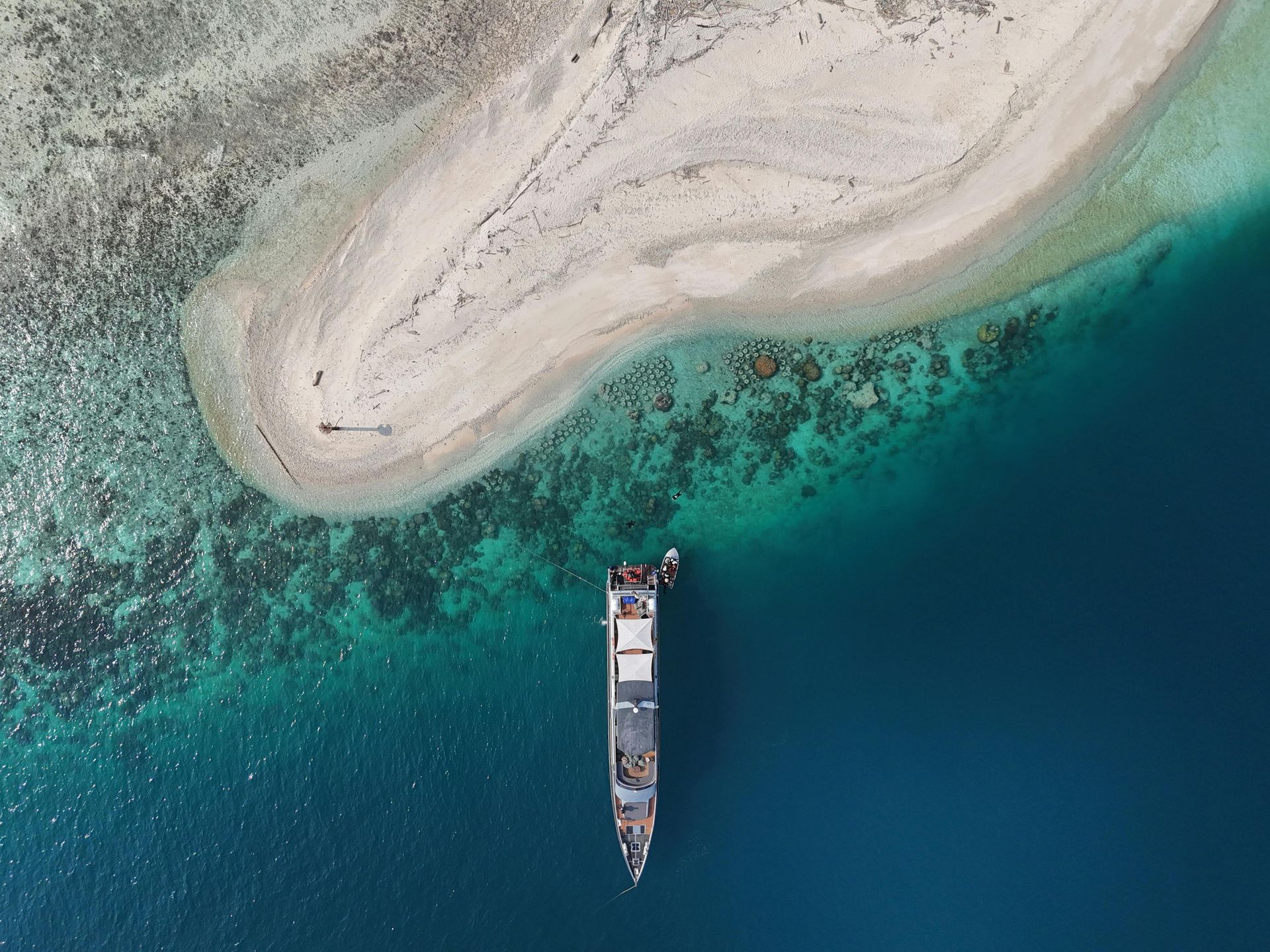 Aerial view of a cargo ship near a white sand island in turquoise water